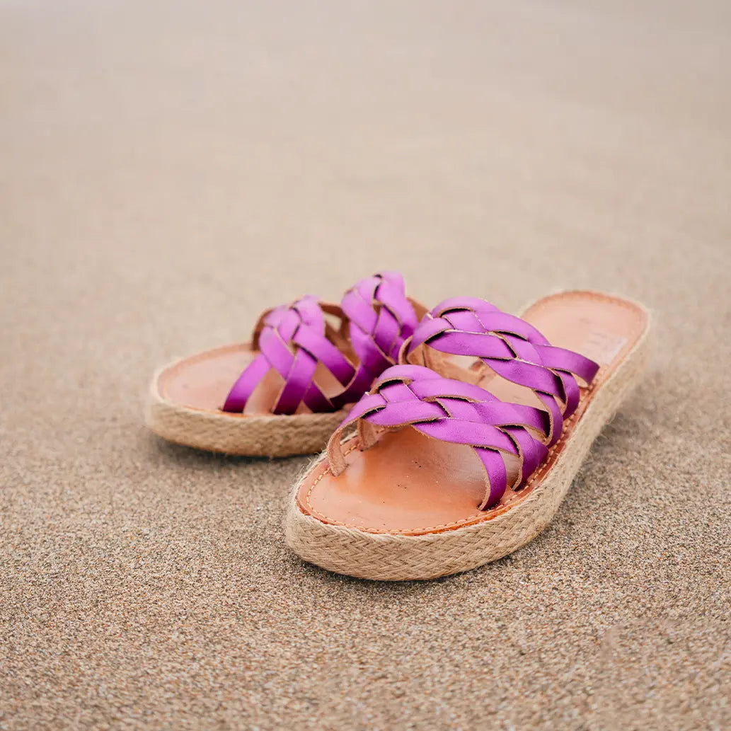 Les Mules Alma Pink Mermaid sont posées sur le sable mouillé.