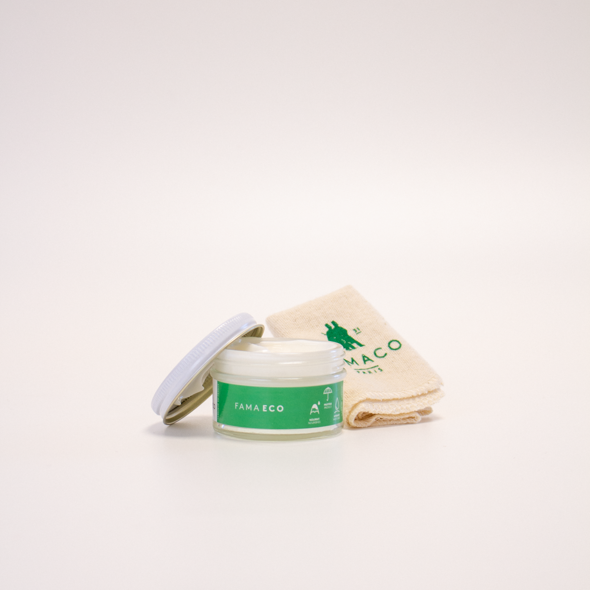 Le pommadier hydratant FAMA ECO de FAMACO est ouvert, avec l’opercule posé sur le contenant. Sa texture est visible, et le chiffon doux fourni est disposé à l’arrière, sur un fond blanc.
