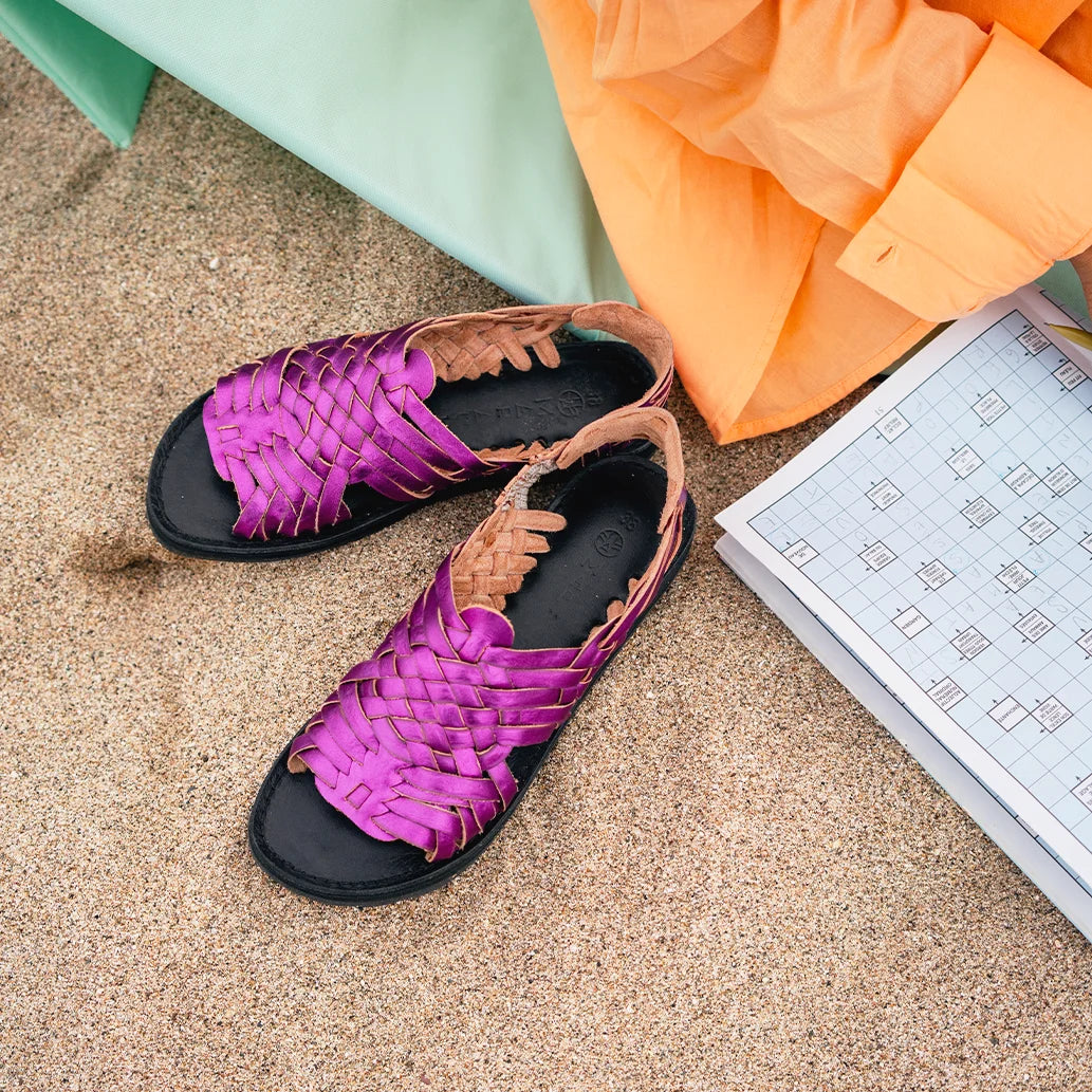 Les Sandales Frida Pink Mermaid sont posées dans le sable à côté d'une femme faisant des mots croisés.