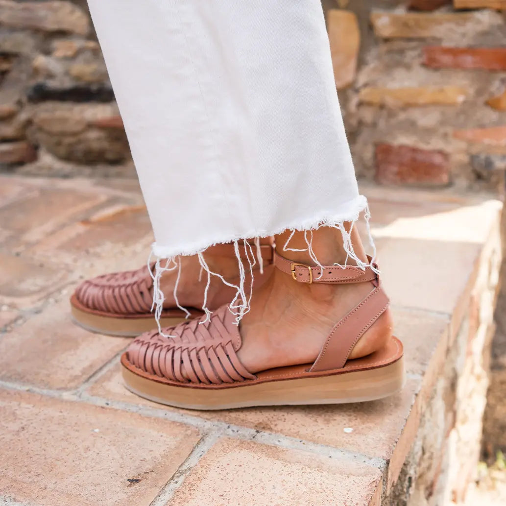 Une femme marche sur un sol en briques avec les Sandales Loma Blush. Elle porte également un jean blanc large effilé.