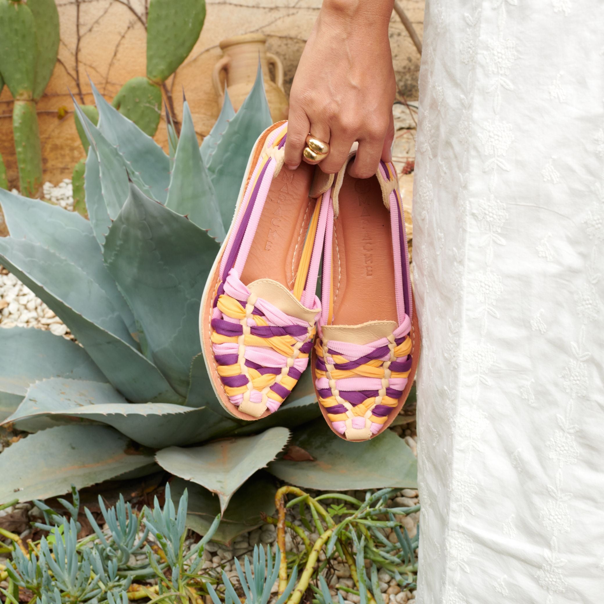 Les mocassins Rita Spring en cuir crème avec tressage en nylon rose, violet et orange, sont tenus à la main par Laura