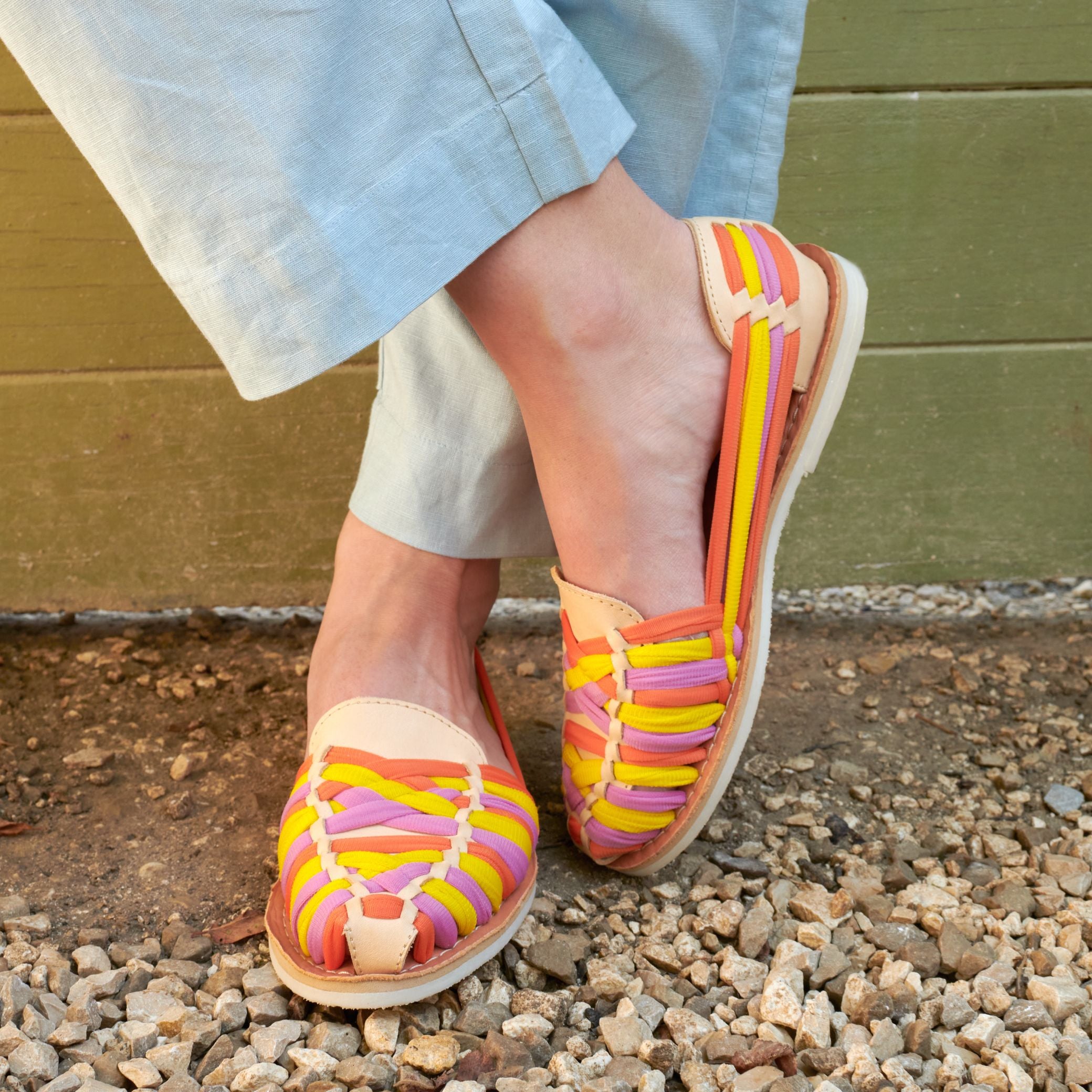 Gros plan sur les mocassins Rita Summer, cuir crème et tressage en nylon jaune, orange et rose, portés aux pieds de Claire.