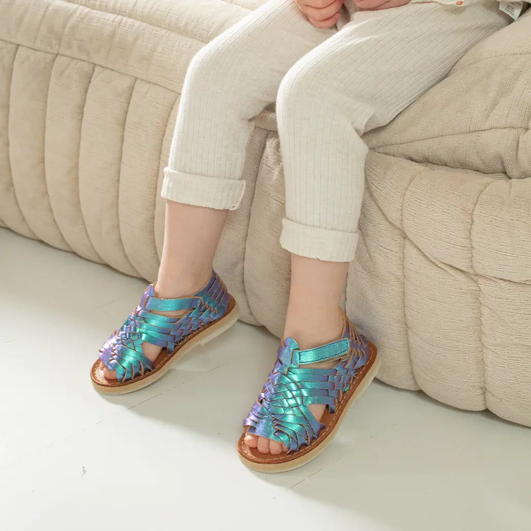 Une petite fille est assise sur un canapé beige et porte les Sandales Sandalita Blue Mermaid ainsi qu'un legging beige côtelé.