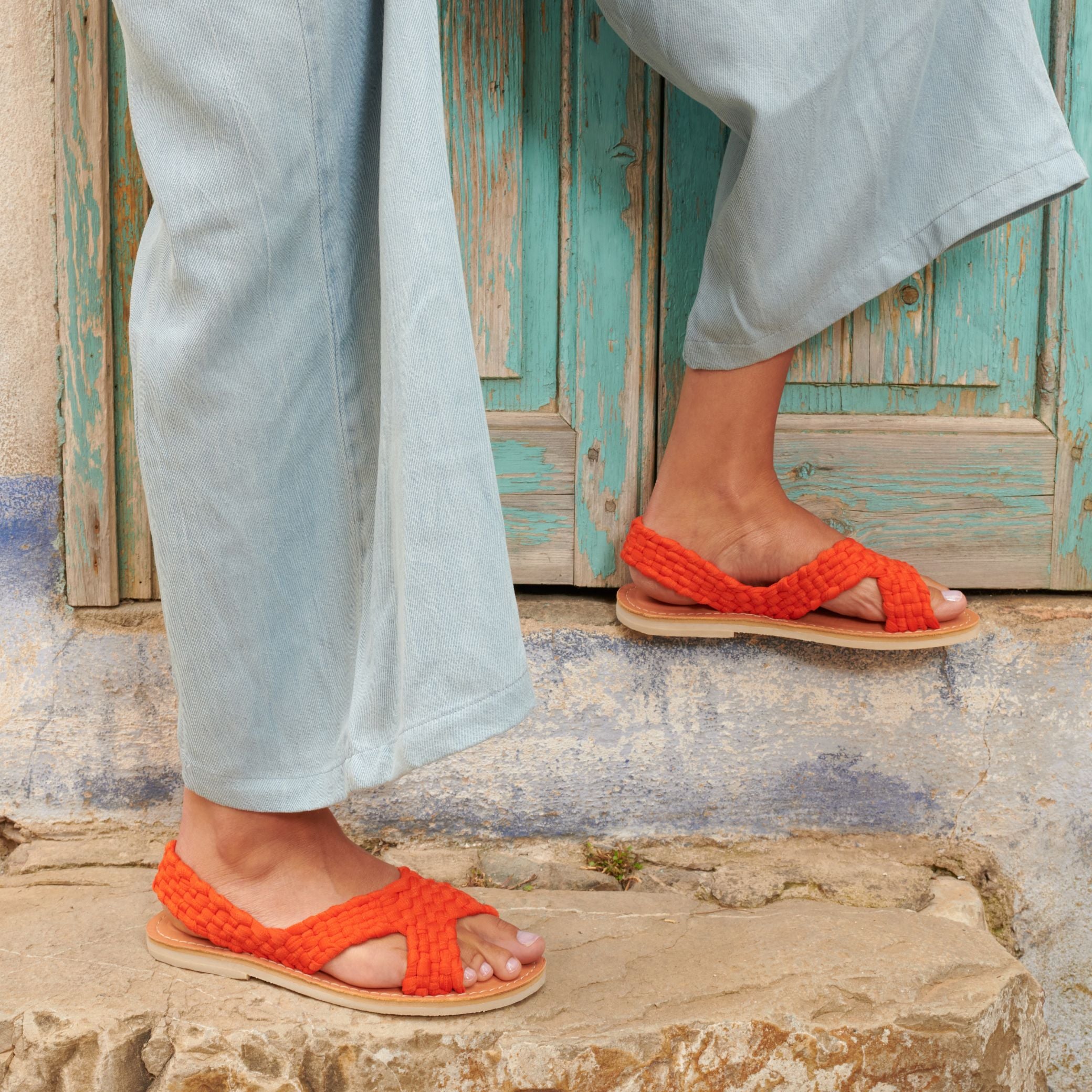 Gros plan sur les sandales Zula Sanguine, au tressage orange, portées aux pieds de Laura.