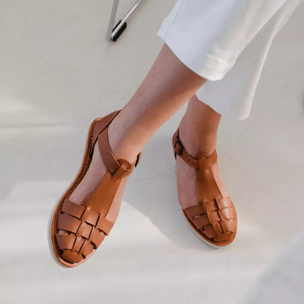 Une femme assise sur fond blanc croise les jambes et porte les Sandales Matilda Camel.