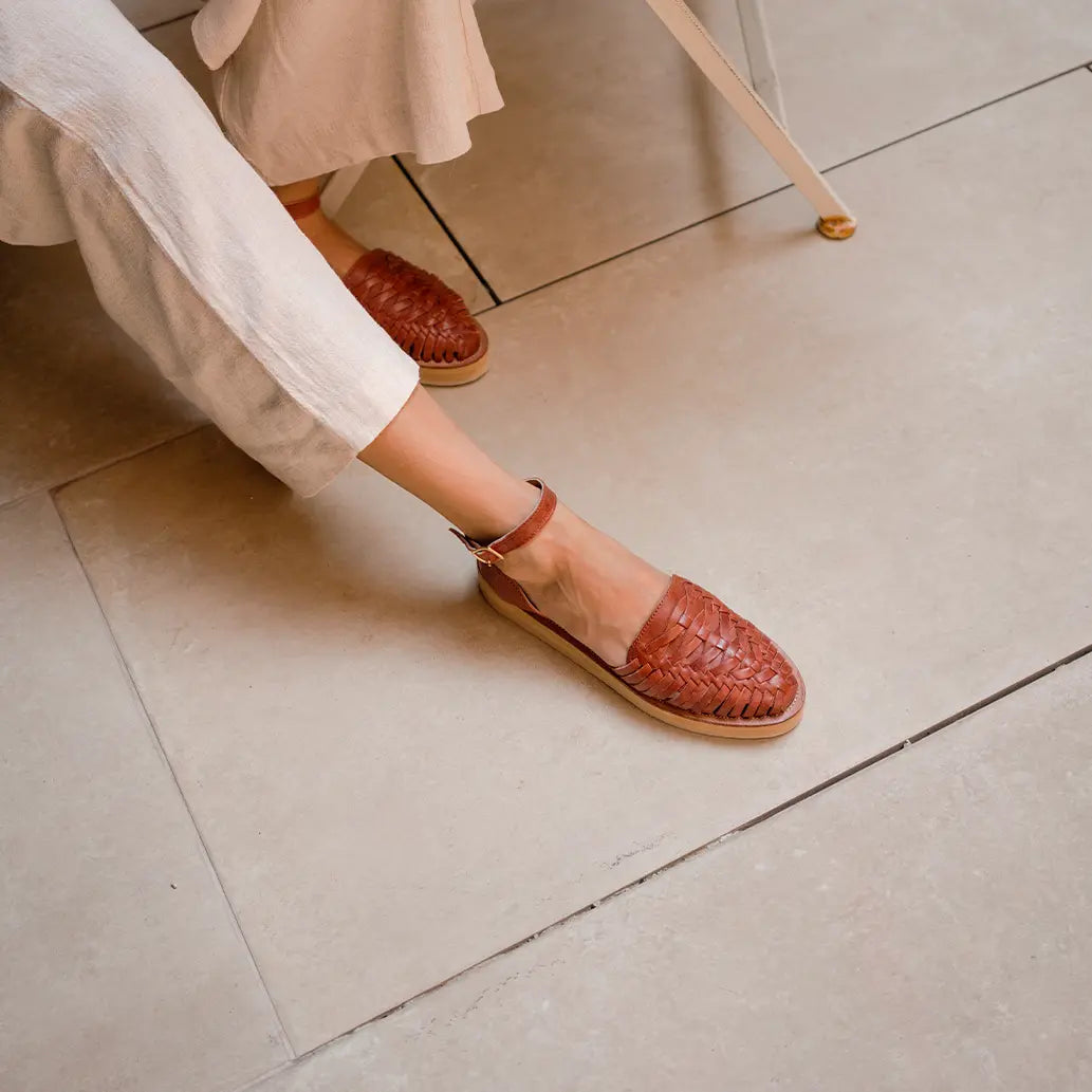Une femme assise sur un carrelage beige porte les Sandales Loma Tabac.