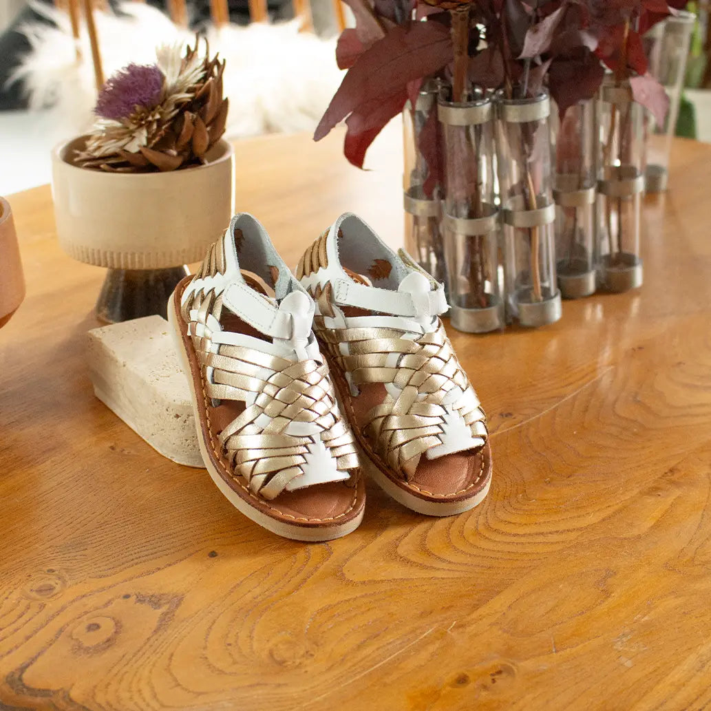 Les Sandales Sandalitas Champagne Blanc sont adossées à un objet de décoration en pierre sur une commode en bois.